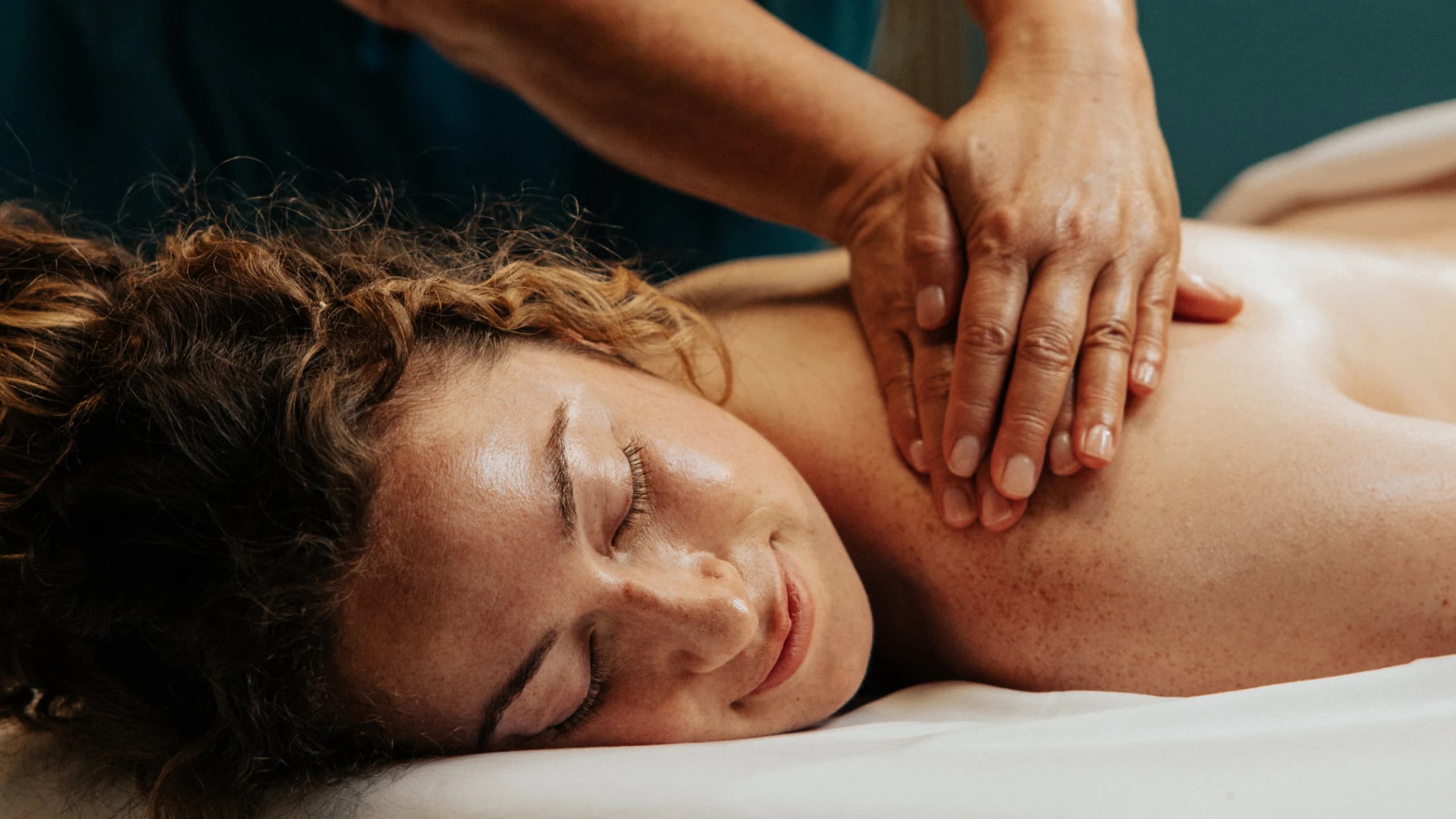 Therapist massaging a woman's shoulders and neck as she relaxes with a soft smile and eyes closed