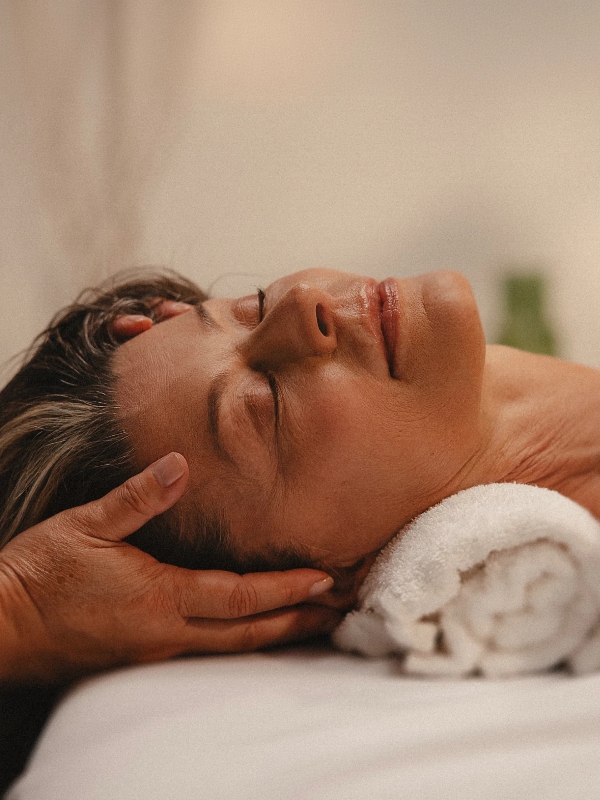 Woman relaxing during a facial and head massage while resting on a soft towel
