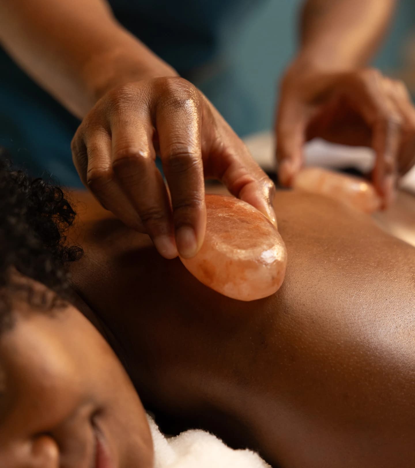 Therapist gliding a warm Himalayan salt stone along a client's back during a therapeutic massage treatment