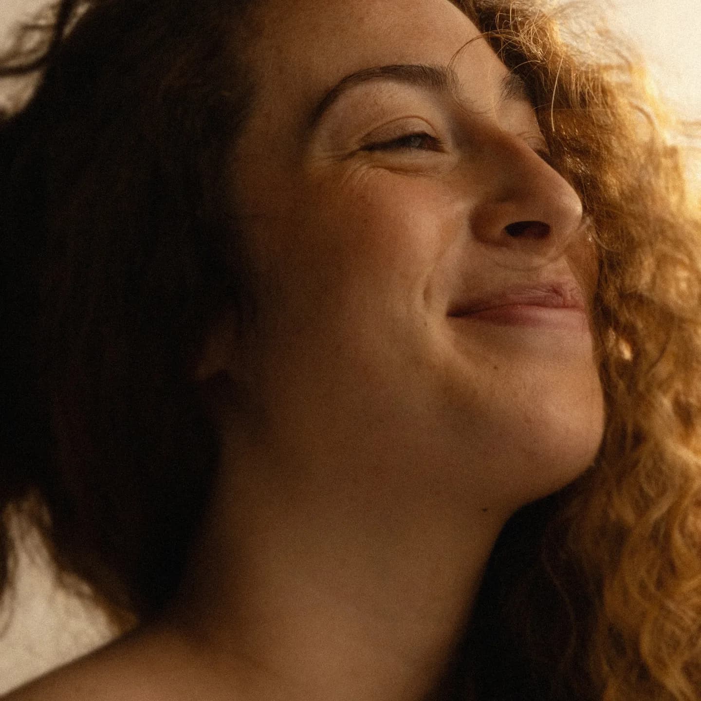 Woman with curly hair smiling warmly in a softly lit spa setting