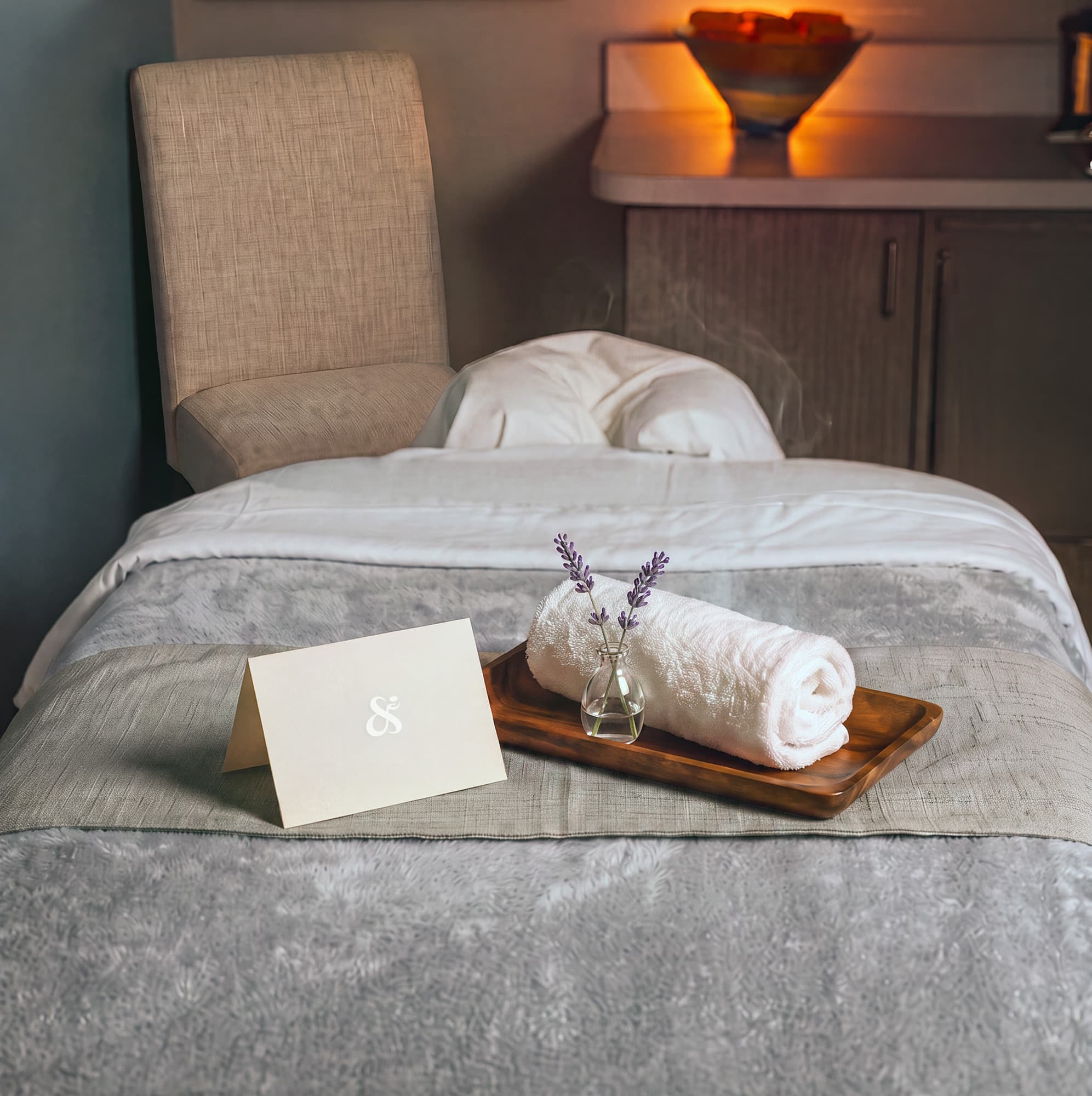 A clean, serene spa treatment room with a massage table, rolled towel, and fresh lavender