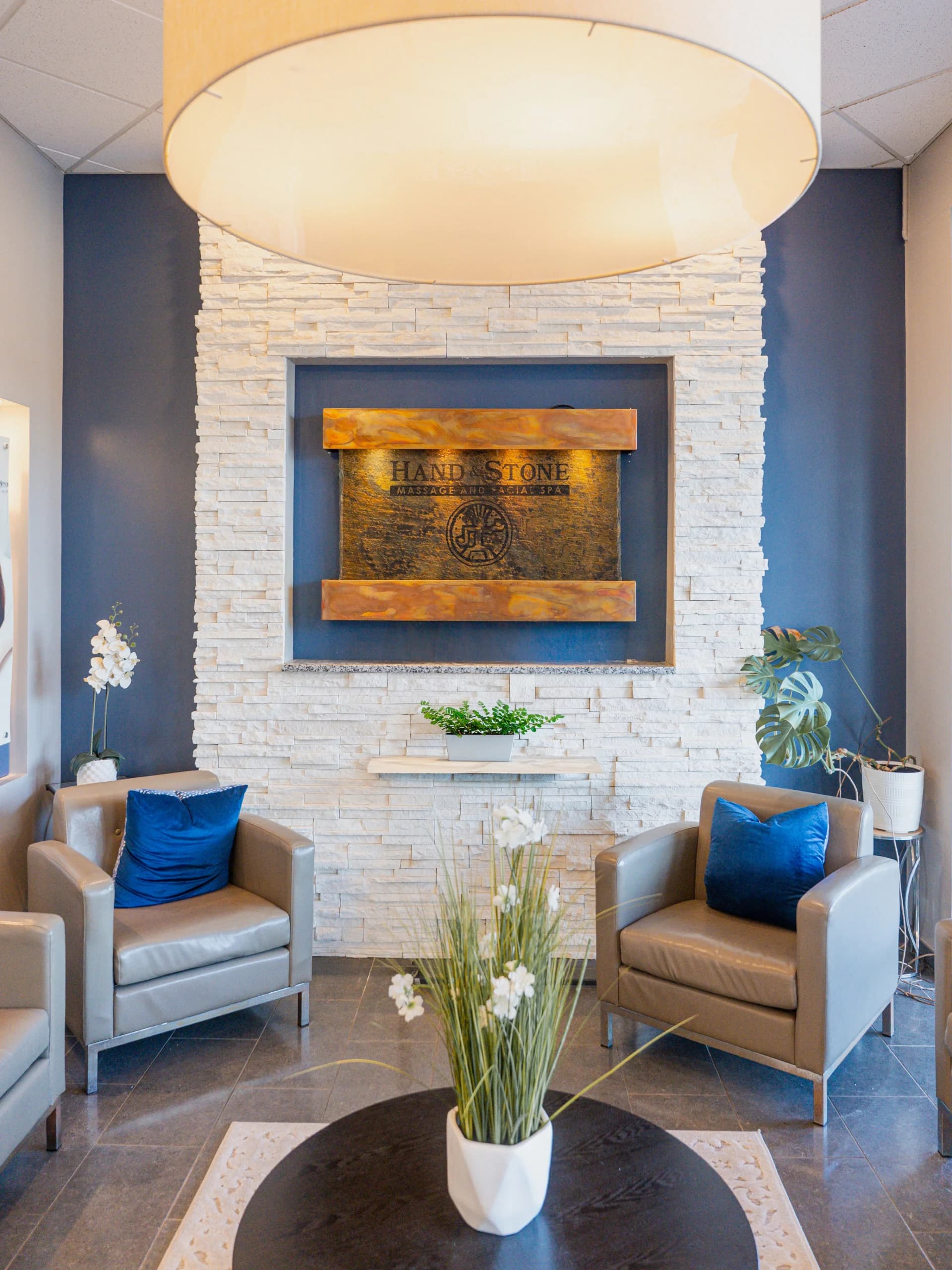Welcoming Hand & Stone spa lobby with soft lighting, stone wall, and comfortable seating