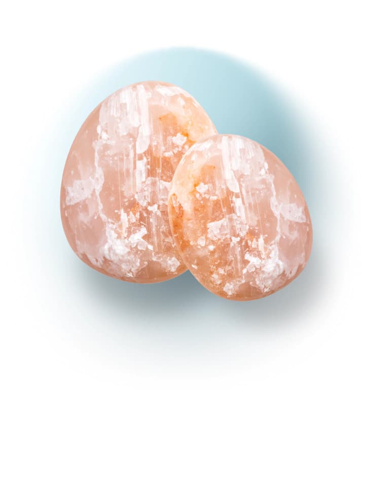 Two pink Himalayan salt stones used as an enhancement to a massage on a light blue background