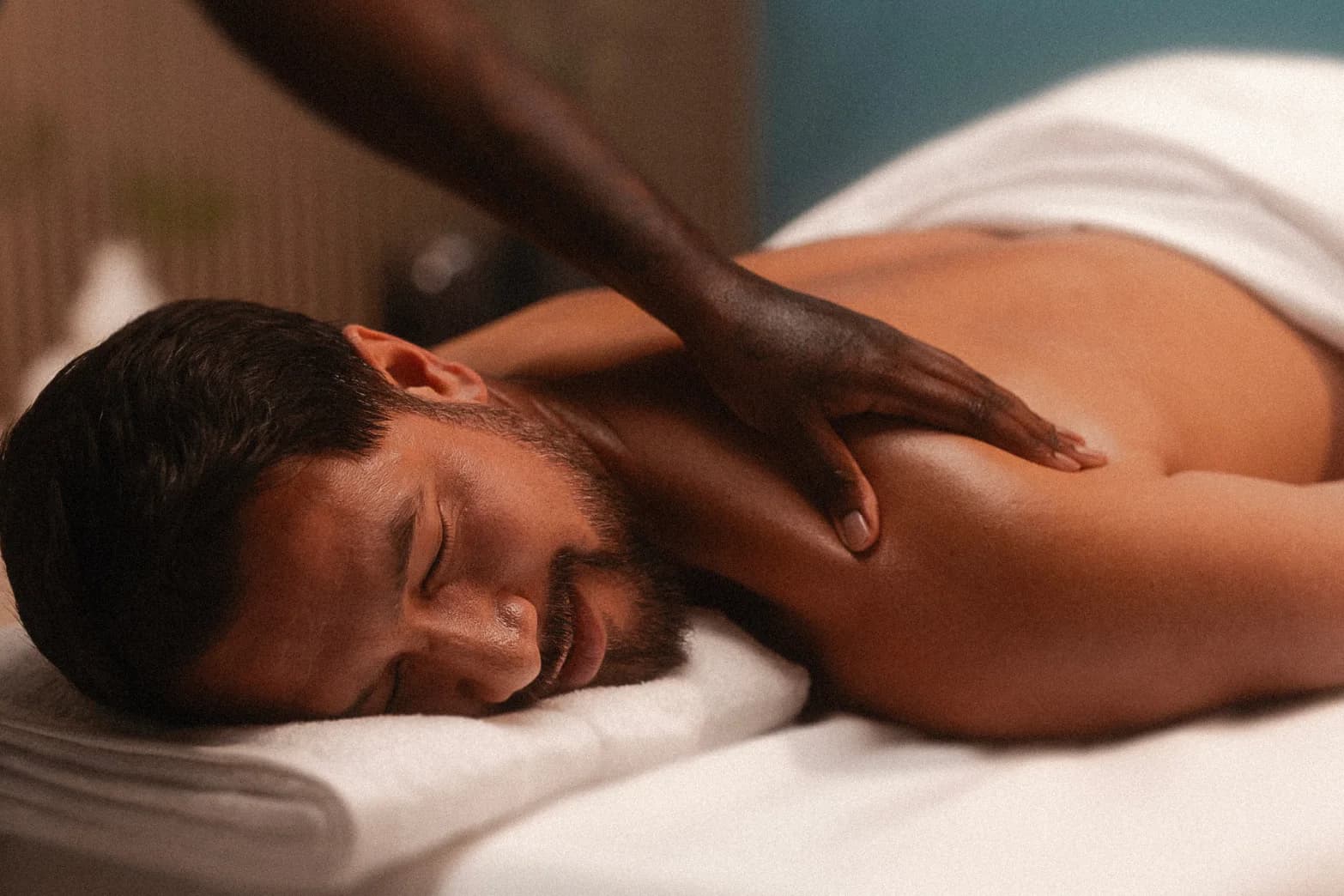 Man lying face down on a massage table, eyes closed, receiving a back massage with a towel draped over them