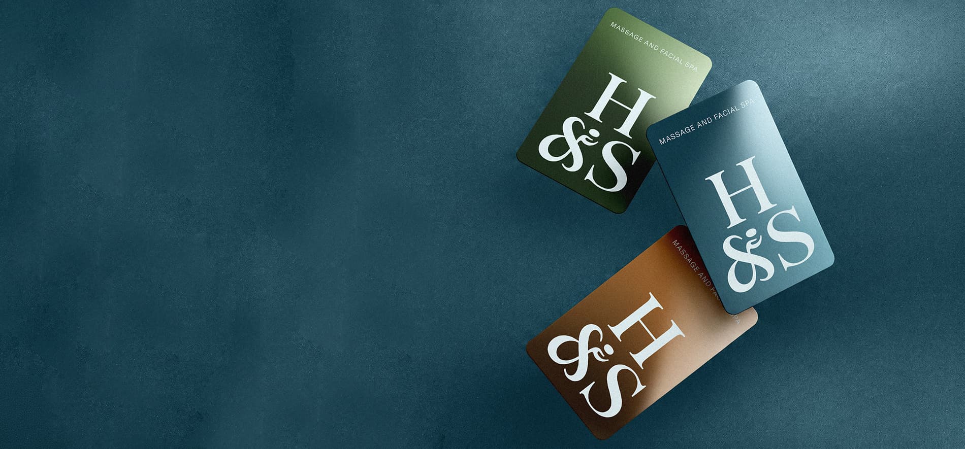 Three Hand & Stone gift cards in green, teal, and copper arranged on a dark background